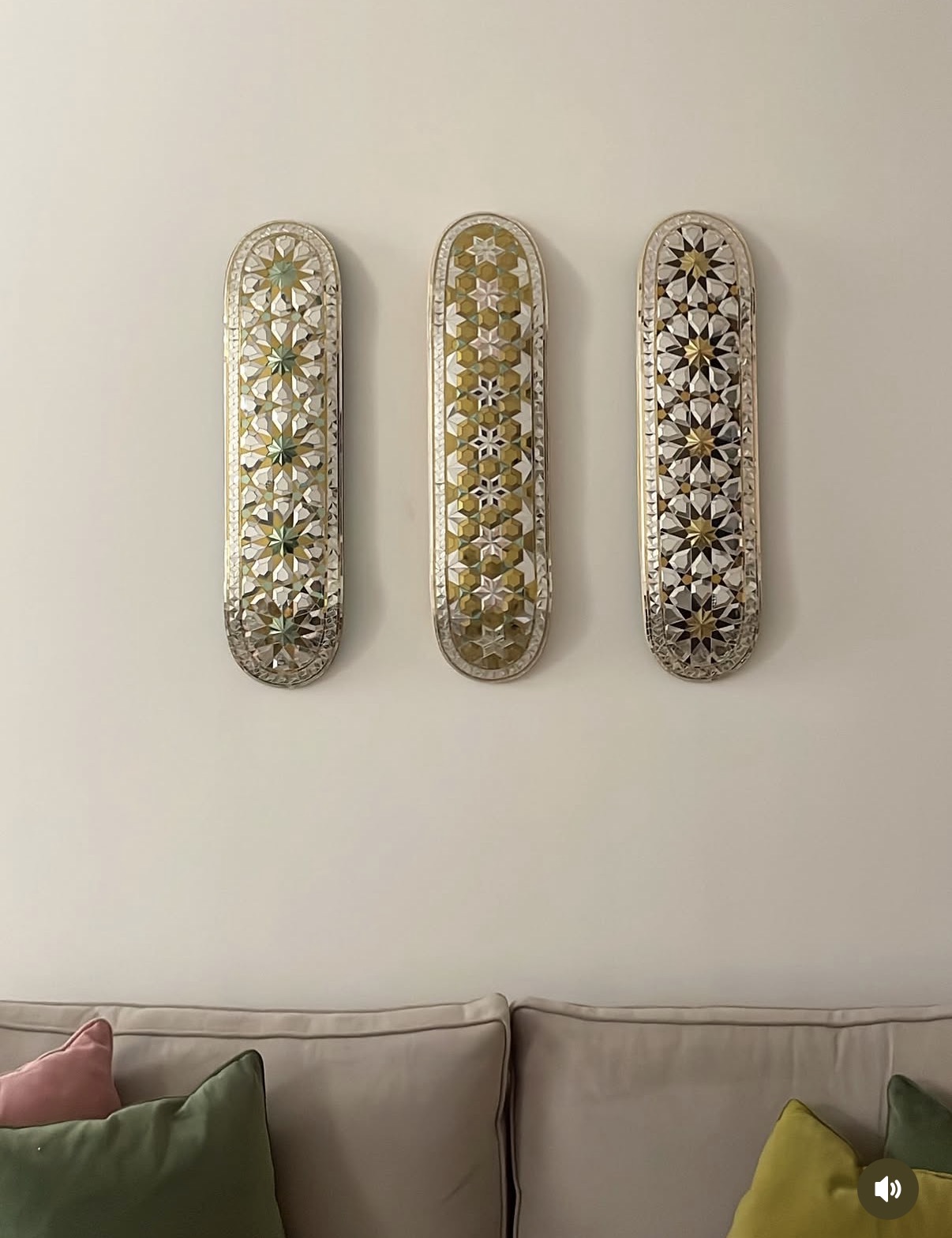 Three skateboard decks covered in geometric Persian mirror mosaic, hung on a wall above a sofa