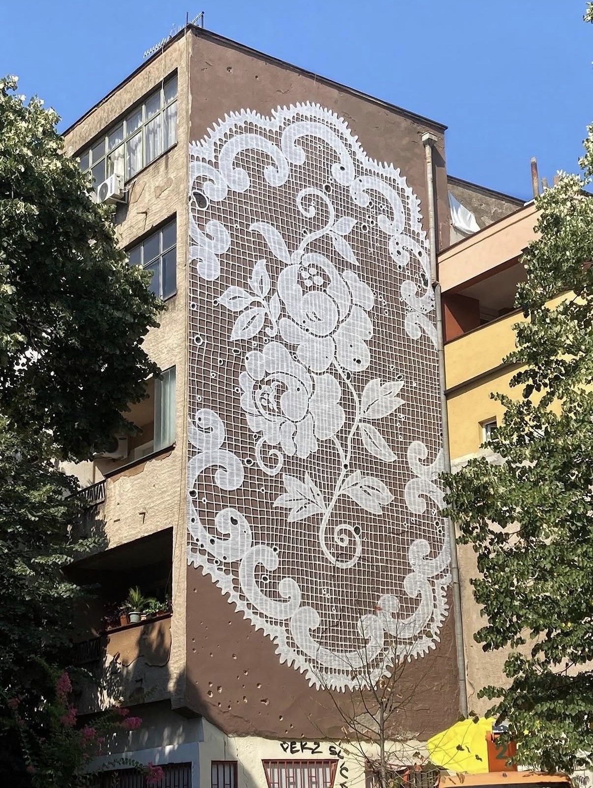 Giant white lace doily painted across the brown side wall of an apartment building