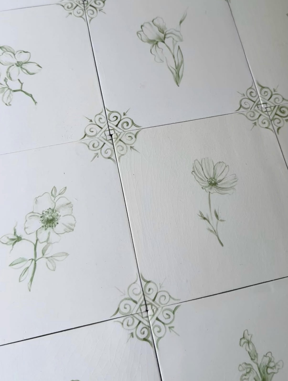 White ceramic tiles hand-painted with green flowers, with scrollwork at the corners